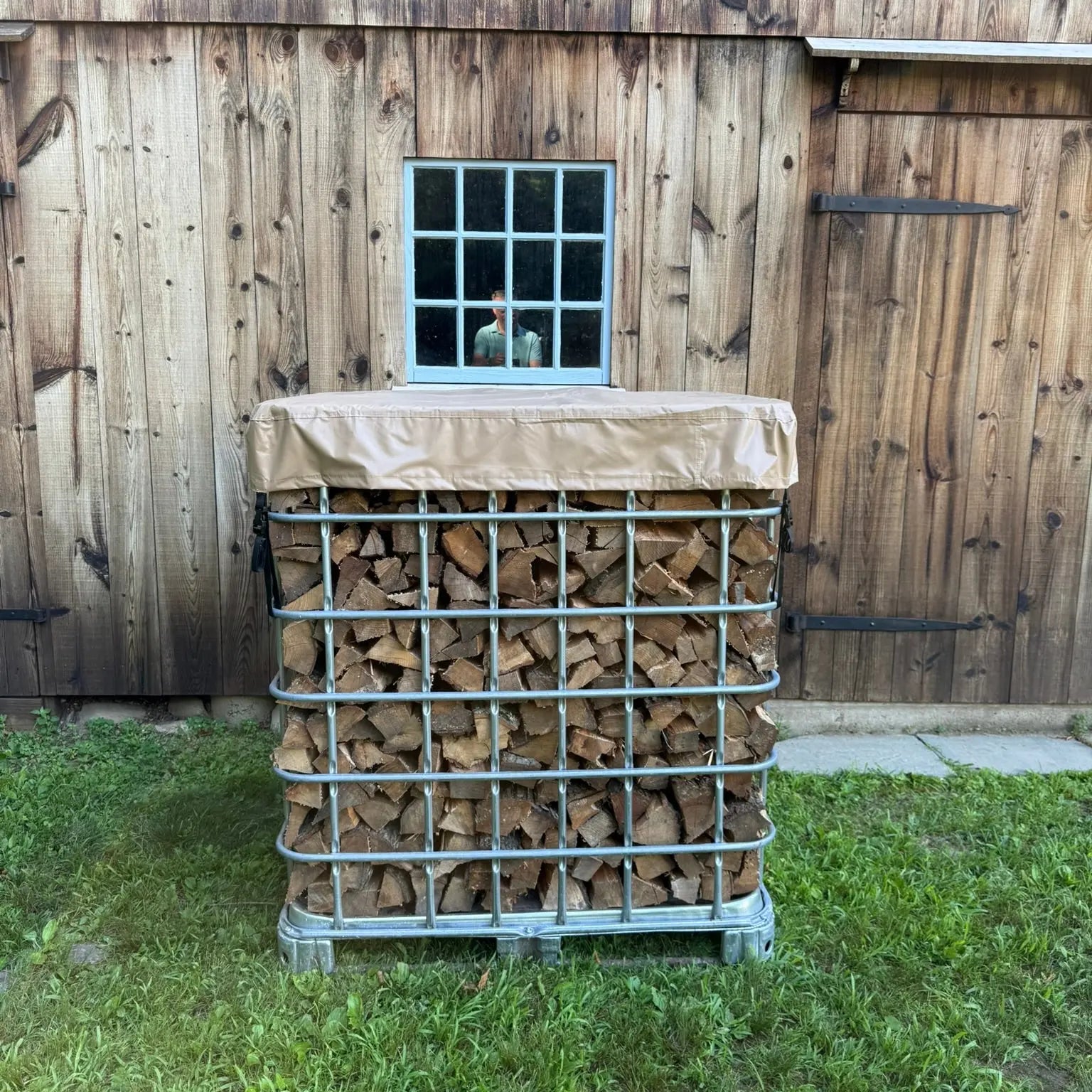 Stack of firewood in a IBC Tote metal cage in front of a barn wall
