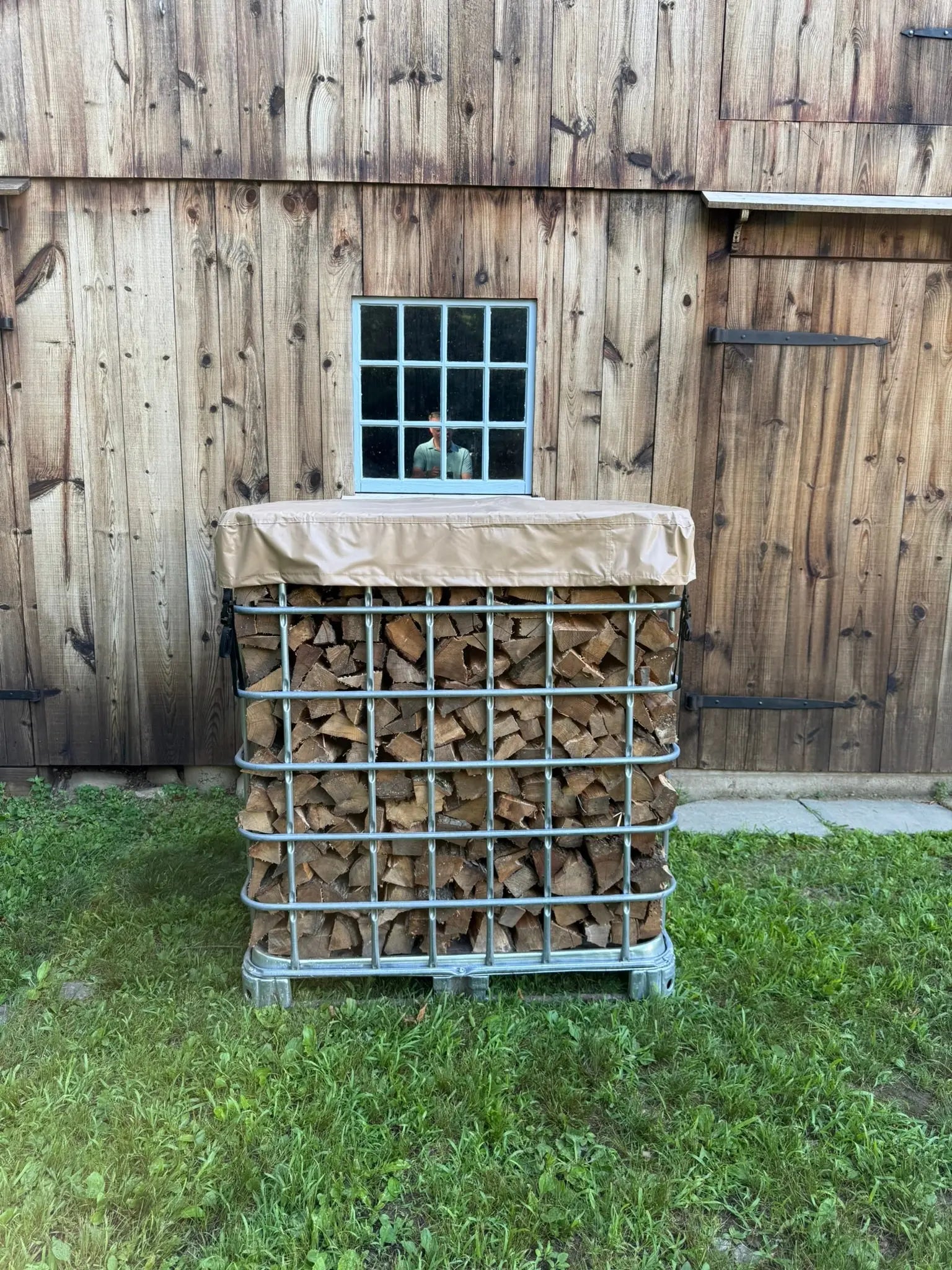 Stack of firewood in a IBC Tote metal cage in front of a barn wall