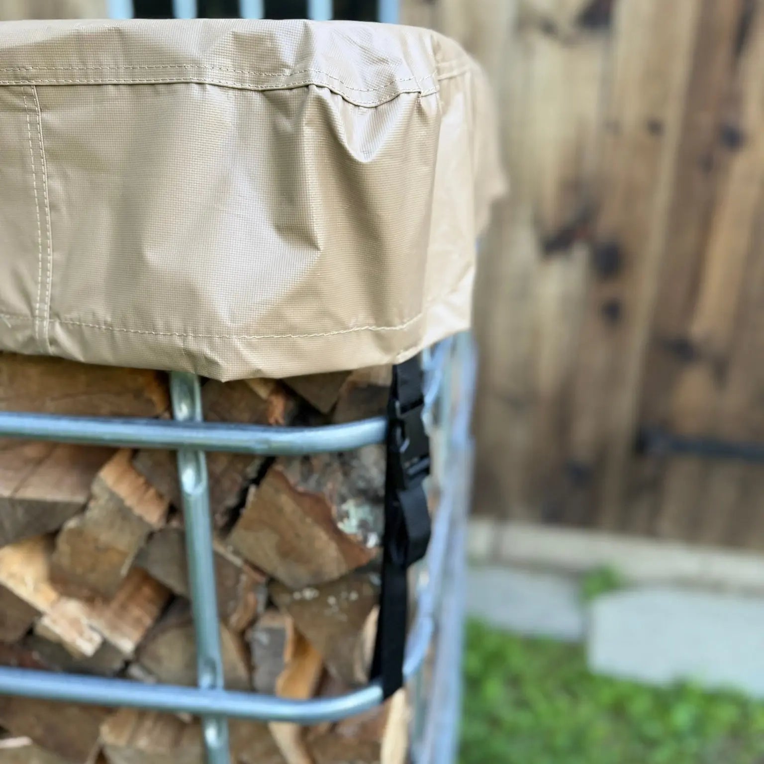 Tan firewood cover on a metal IBC tote firewood rack with stacked firewood inside, against a wooden barn background.
