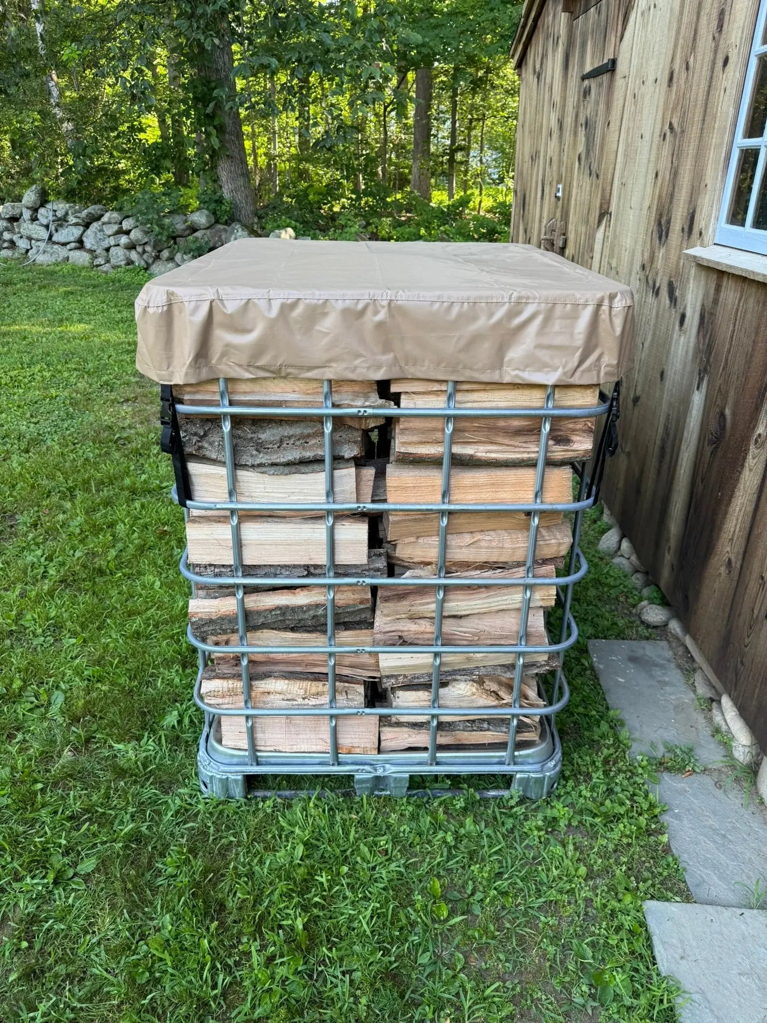 Stack of firewood inside a IBC tote with a cordwood cover tarp on top in an outdoor setting.